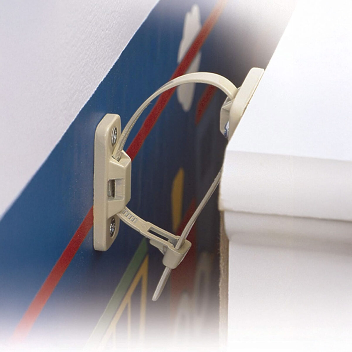Close-up view of Mommy's Helper Anti-Tip Furniture Safety Strap installed between a wall and a dresser, preventing tipping.