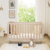 Front view of Babymore Dante Cot Bed in cashmere wood finish, styled in a bright nursery.
