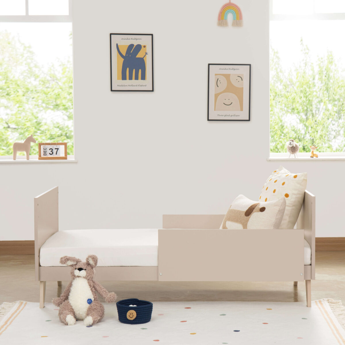 Side view of Babymore Dante Cot Bed as toddler bed with playful pillows and plush toy.