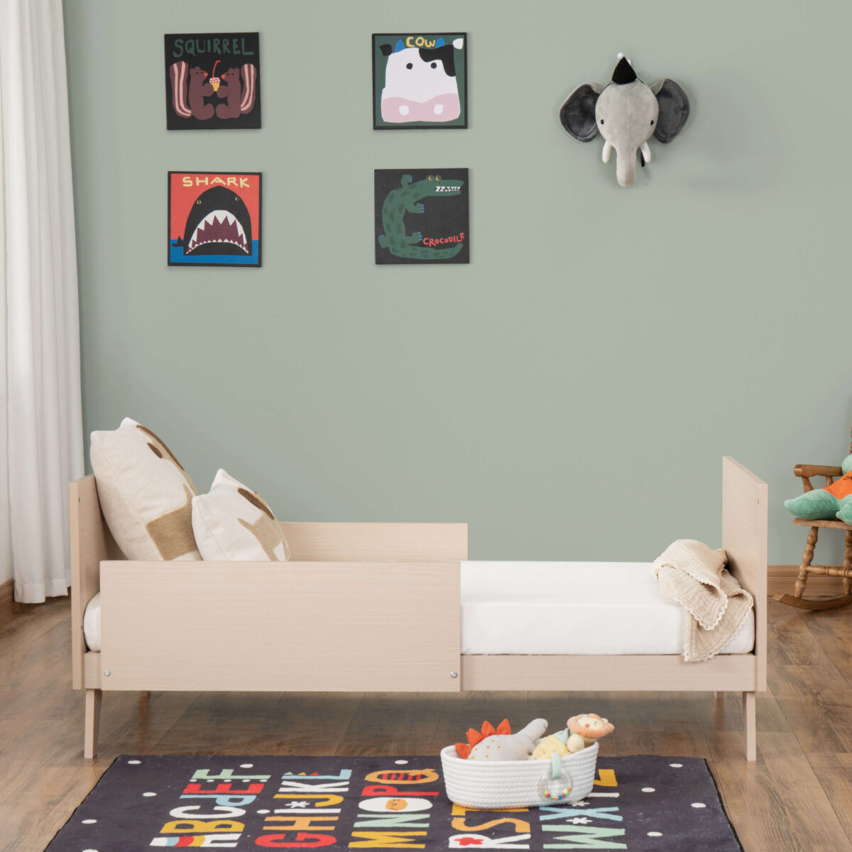 Side view of Babymore Dante Cot Bed converted to toddler bed with cozy bedding and blanket.