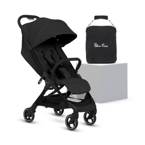 A sleek, all-black baby stroller from Silver Cross, featuring a quilted seat, adjustable canopy, and five-point harness. The stroller has a black frame with matching black handlebars. A black travel bag with the "Silver Cross" logo sits on a white platform beside it.