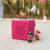 Pink Toniebox with Skye on top and Chase and Marshall beside it, kids playing jump rope in background