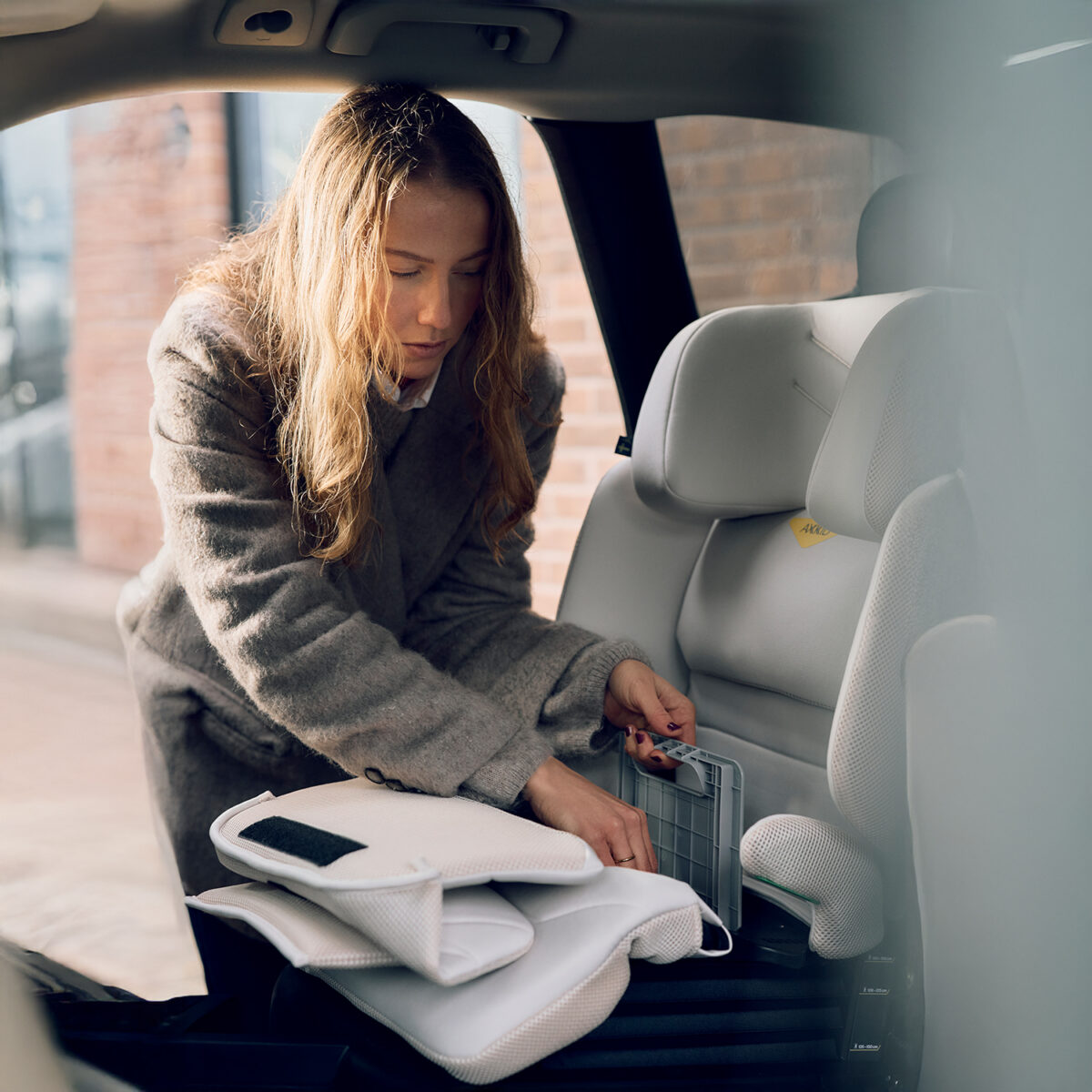 Woman adjusting components of the AXKID Up High Back Booster Car Seat during installation.
