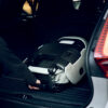 AXKID Up High Back Booster Car Seat being lifted into a vehicle trunk in its folded and portable form.