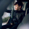 Young boy sitting calmly in the AXKID Up High Back Booster Car Seat, hands in hoodie pockets.