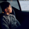 Side profile of a boy seated in AXKID Up High Back Booster Car Seat, looking out a car window.