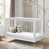 White cot bed with acrylic slats, soft toys inside, in a modern nursery with panelled walls.