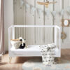 Cot bed converted to toddler bed with soft toys and blanket, under bunting and pendant light.