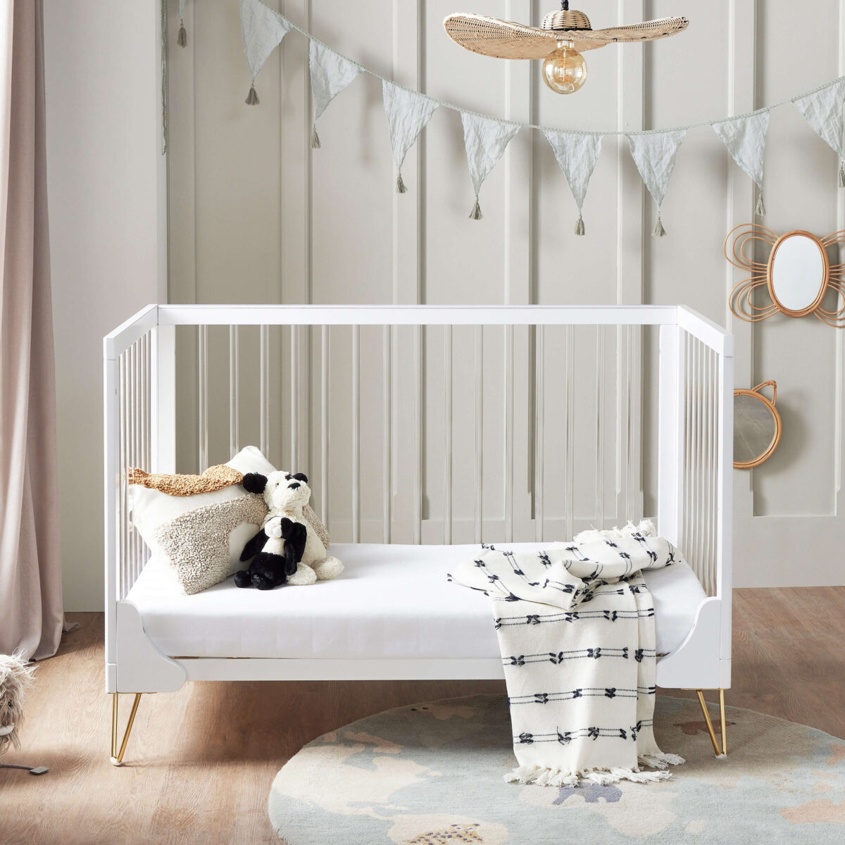 Cot bed converted to toddler bed with soft toys and blanket, under bunting and pendant light.
