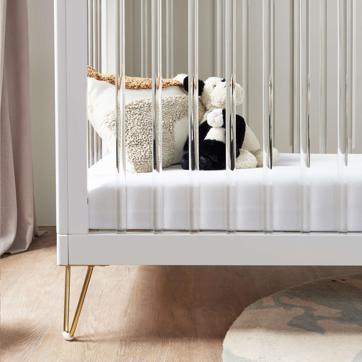 Close-up of plush toys through the acrylic slats of a white cot bed on wooden flooring.