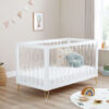 White acrylic cot bed with gold legs, styled in a bright nursery with soft toys and cushions.