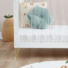 Close-up of acrylic slats, mint flower cushion, and woven pear-shaped basket beside cot bed.