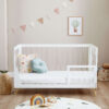 Cot bed converted to toddler bed with one side removed, featuring pastel pillows and decor.