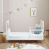Toddler bed setup with low side rails and playful nursery backdrop including bunting and toys.