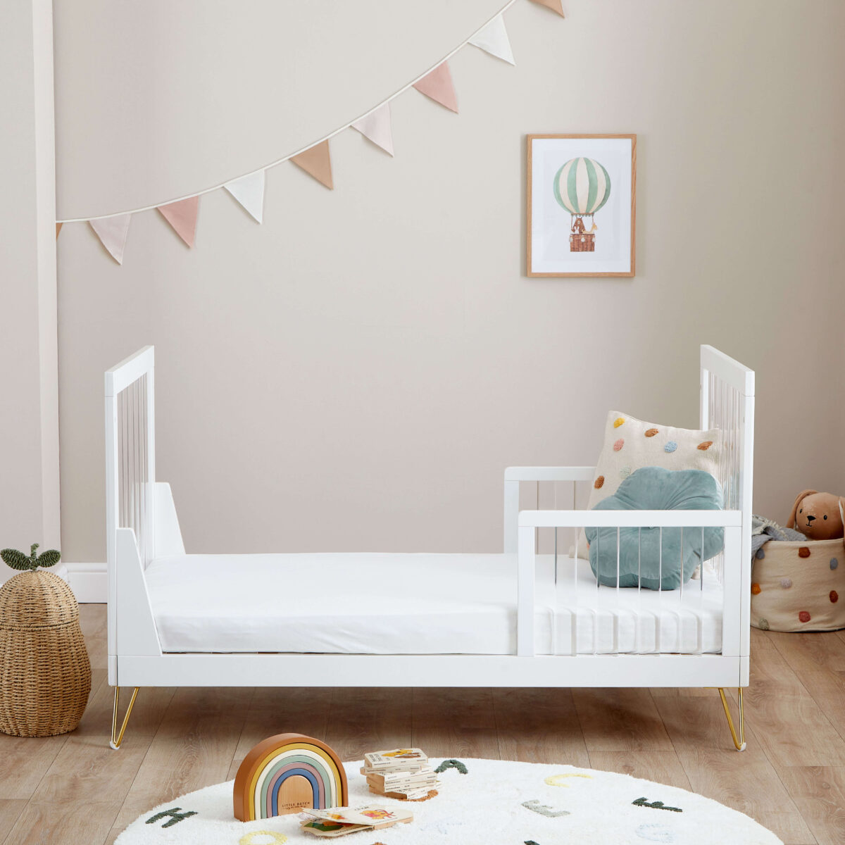 Toddler bed setup with low side rails and playful nursery backdrop including bunting and toys.