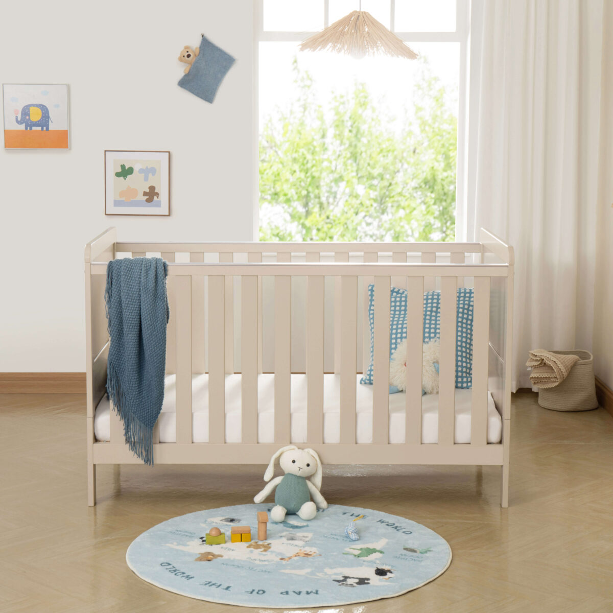 Front view of cashmere cot bed with bunny plush, blue pillows and toys.