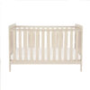 Front-facing view of cot bed in cashmere with white mattress against white background.