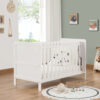 White cot bed in modern nursery with panda plush, round rug and wooden flooring.