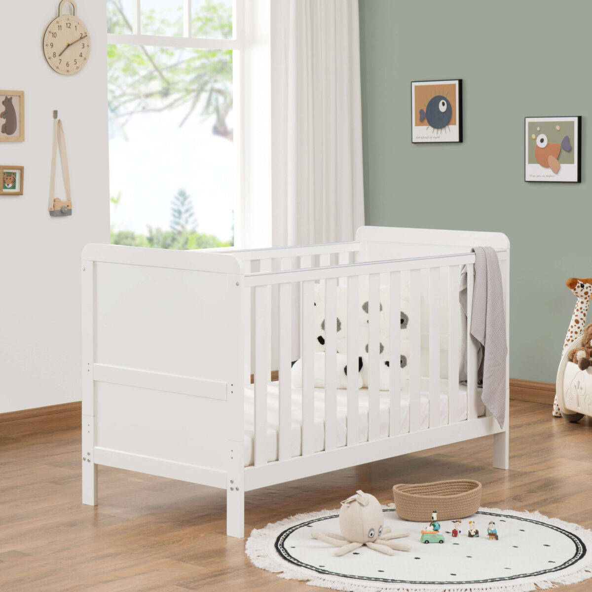 White cot bed in modern nursery with panda plush, round rug and wooden flooring.