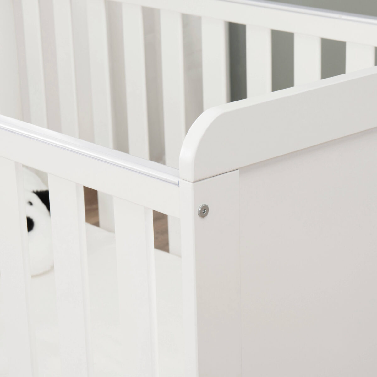 Close-up of cot bed corner showing smooth white finish and assembly detail.