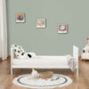 White toddler bed with toys, pillow and grey blanket in cozy nursery setting.
