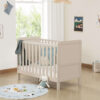 Cashmere cot bed near window with plush toys, blue rug and nursery wall art.