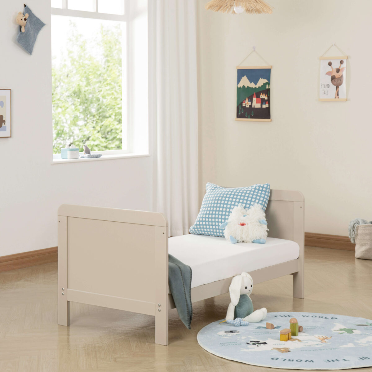 Toddler bed setup in cashmere with blue pillow, soft toy and natural light.