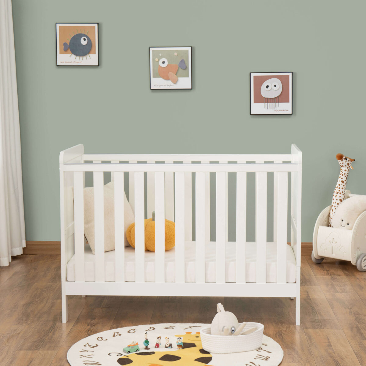 White mini cot bed in nursery with toys, pumpkin pillow and wall art above.