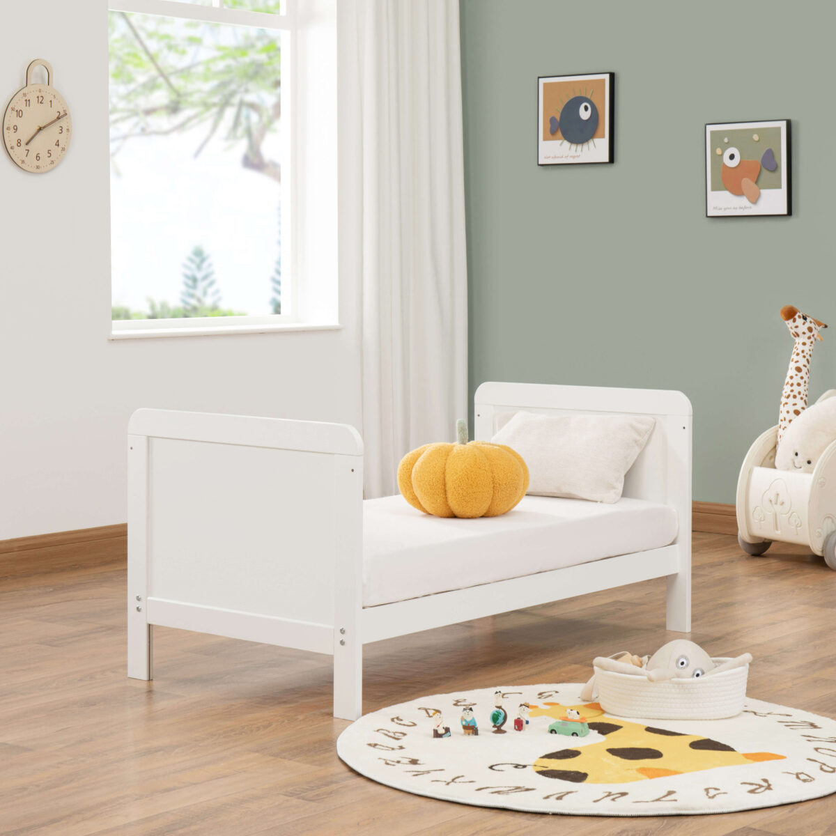 White toddler bed setup with pumpkin pillow, toys and soft natural light.