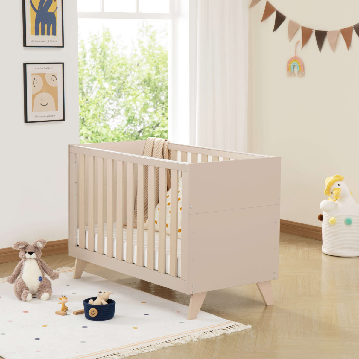 Angled view of Babymore Dante Mini Cot Bed in cashmere styled with plush toys and soft decor.