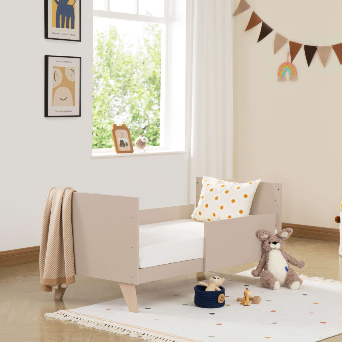 Babymore Dante Mini Cot Bed as toddler bed with blanket and cushion in warm-toned nursery.