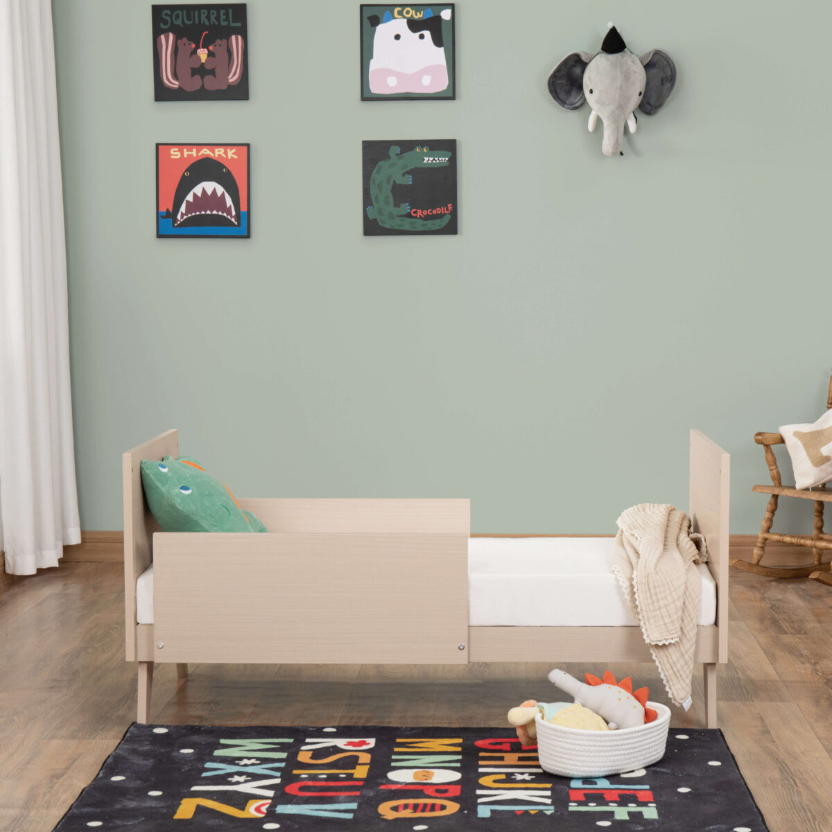 Side view of Babymore Dante Mini Cot Bed in toddler mode with comfy bedding and rug.
