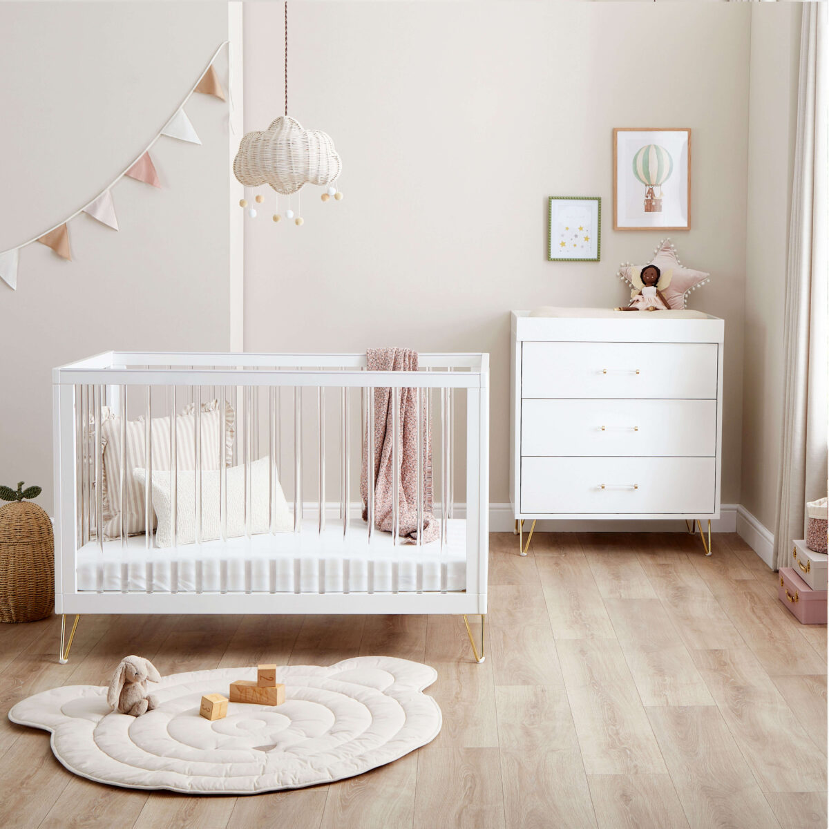 White crib and dresser set in a soft-toned nursery with cloud mobile and pastel bunting.