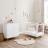Bright nursery with white crib, dresser, bunting, and cloud light beside a large window.