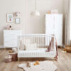 White cot bed, dresser, and wardrobe in a soft-toned nursery with plush toys and wall decor.