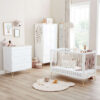 Bright nursery with white furniture set, soft rug, and large windows letting in natural light.