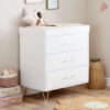 White dresser with three drawers and gold handles, styled with a doll and soft neutral decor.
