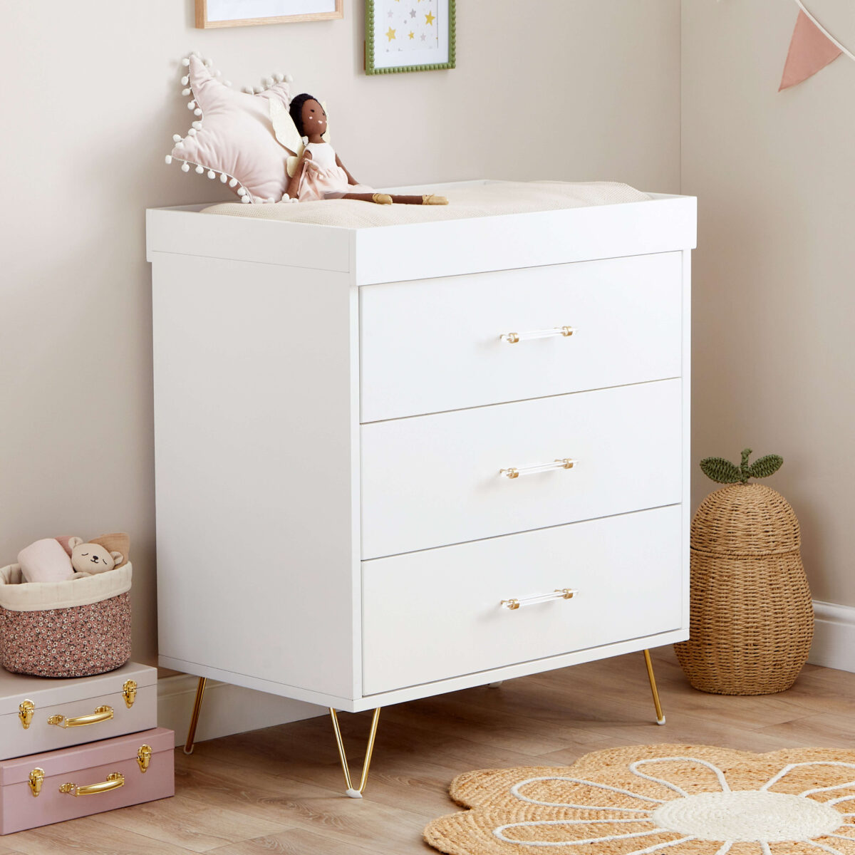 White dresser with three drawers and gold handles, styled with a doll and soft neutral decor.