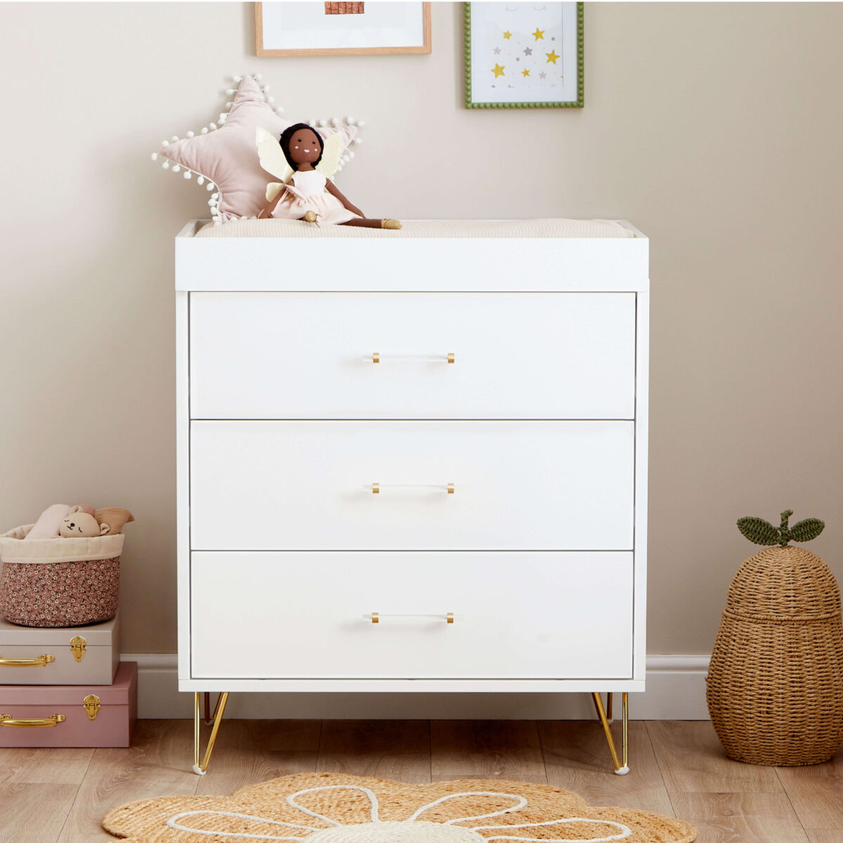 White chest changer with gold legs and doll on top, next to a star pillow and wall art.
