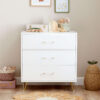 Dresser with books, toys, and decorative items on top, framed by neutral nursery decor.