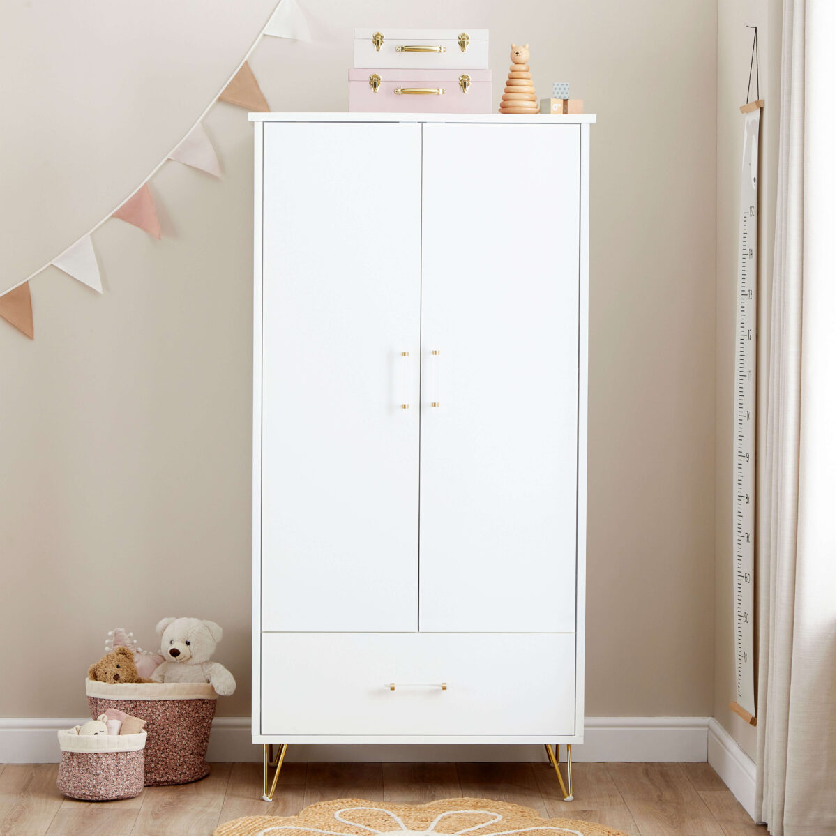 White wardrobe with gold legs in a nursery, decorated with toys, bunting, and baskets.