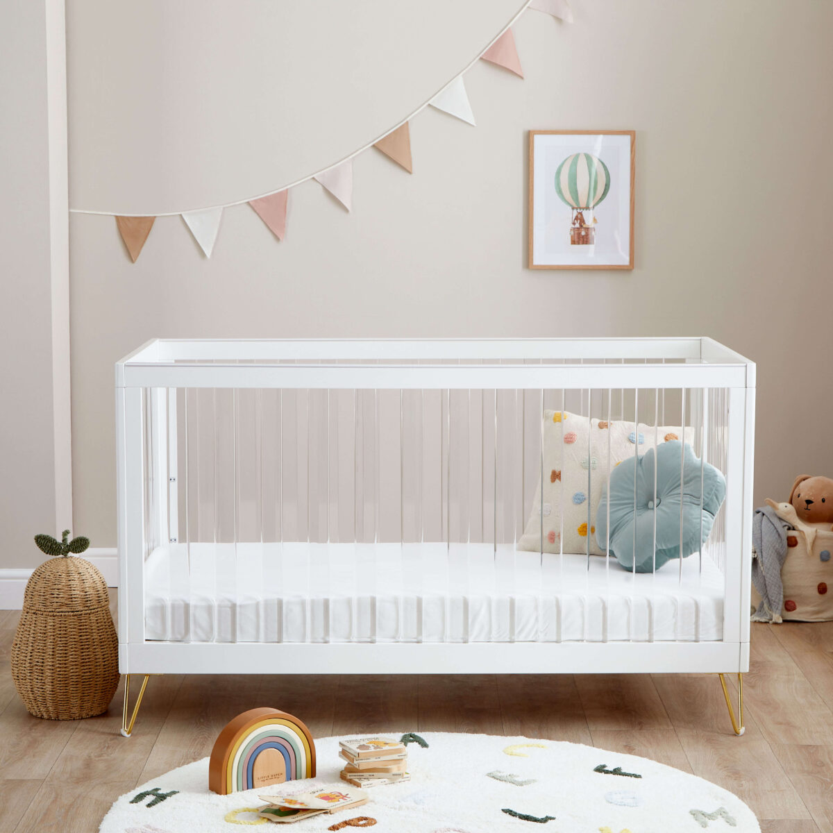 Minimalist white crib with cushions, rainbow toy, and pastel bunting on the wall.