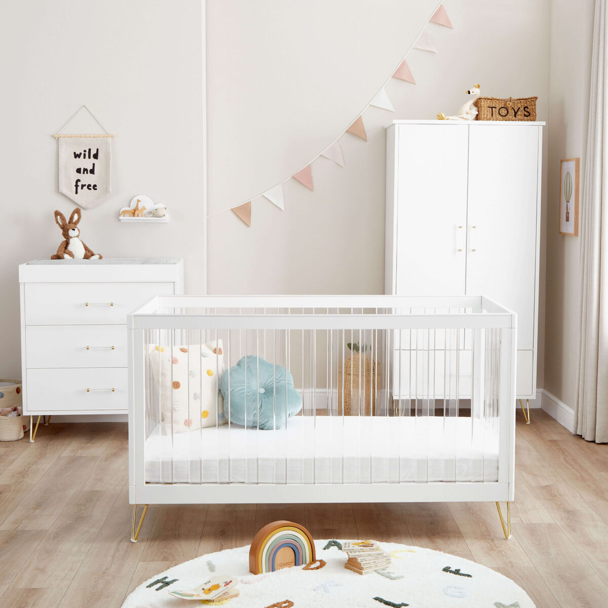 White crib, dresser, and wardrobe in a cozy nursery with pastel bunting and soft toys.